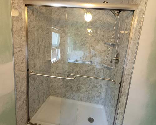 Walk-in shower with marble-look wall panels, glass doors, and built-in bench