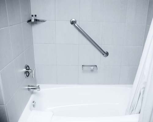 White bathtub with gray tile wall surround, grab bar, and chrome fixtures