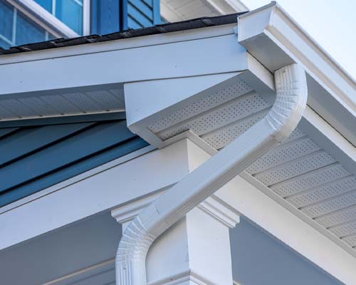 White seamless gutter and downspout on home corner with blue siding